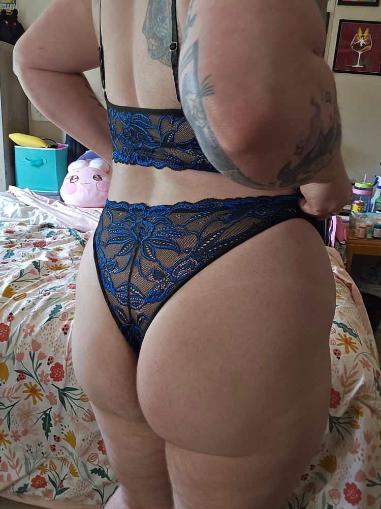 Bee wearing a black and blue lace bra and panty set, facing away from the camera to show their butt 