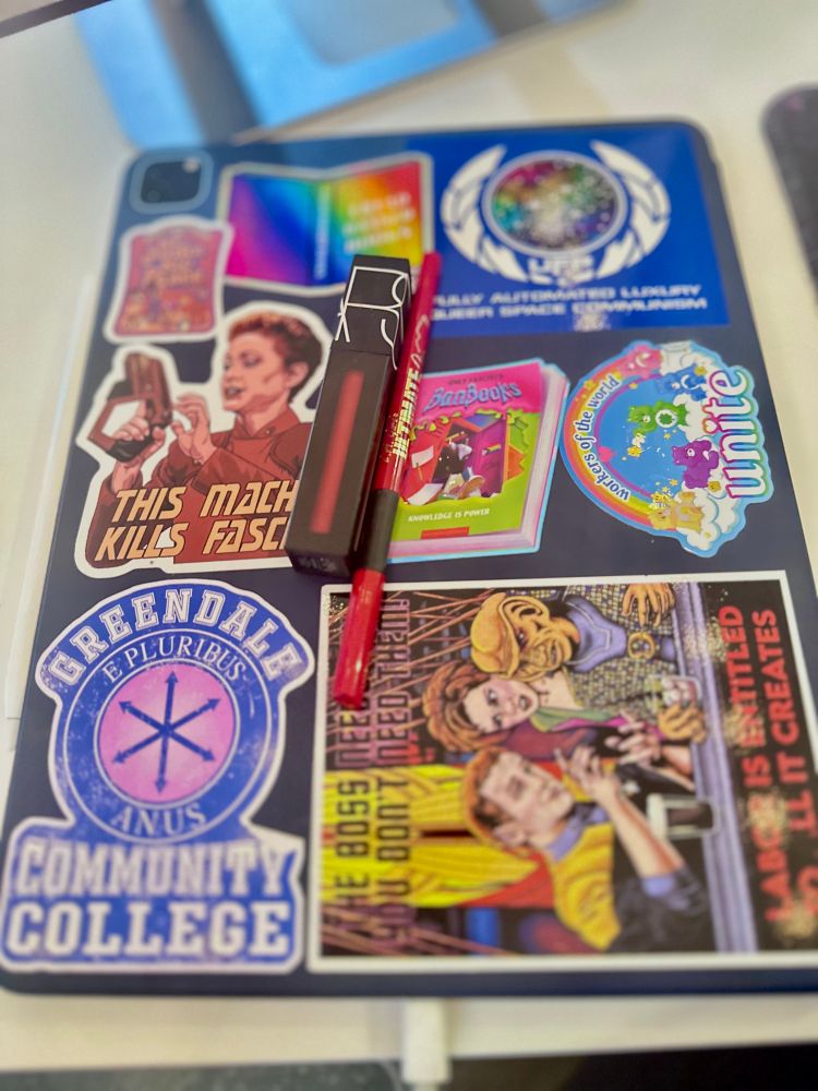An iPad covered in stickers with leftist and Star Trek themes with NARS Lipstick in Starwoman and L.A. Girl lipliner in Red 