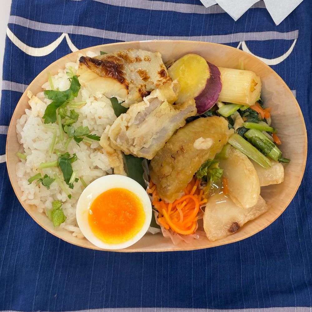 蓮根の挟み揚げ、助惣鱈の塩麹漬け焼き、焼いた蕪のあんかけ、にんじんのラペ、小松菜の和え物、極細のきんぴらごぼう、さつまいも甘煮、ゆで卵、ごはんは生姜ごはん。弁当箱は経木のわっぱ、バランが笹の葉。