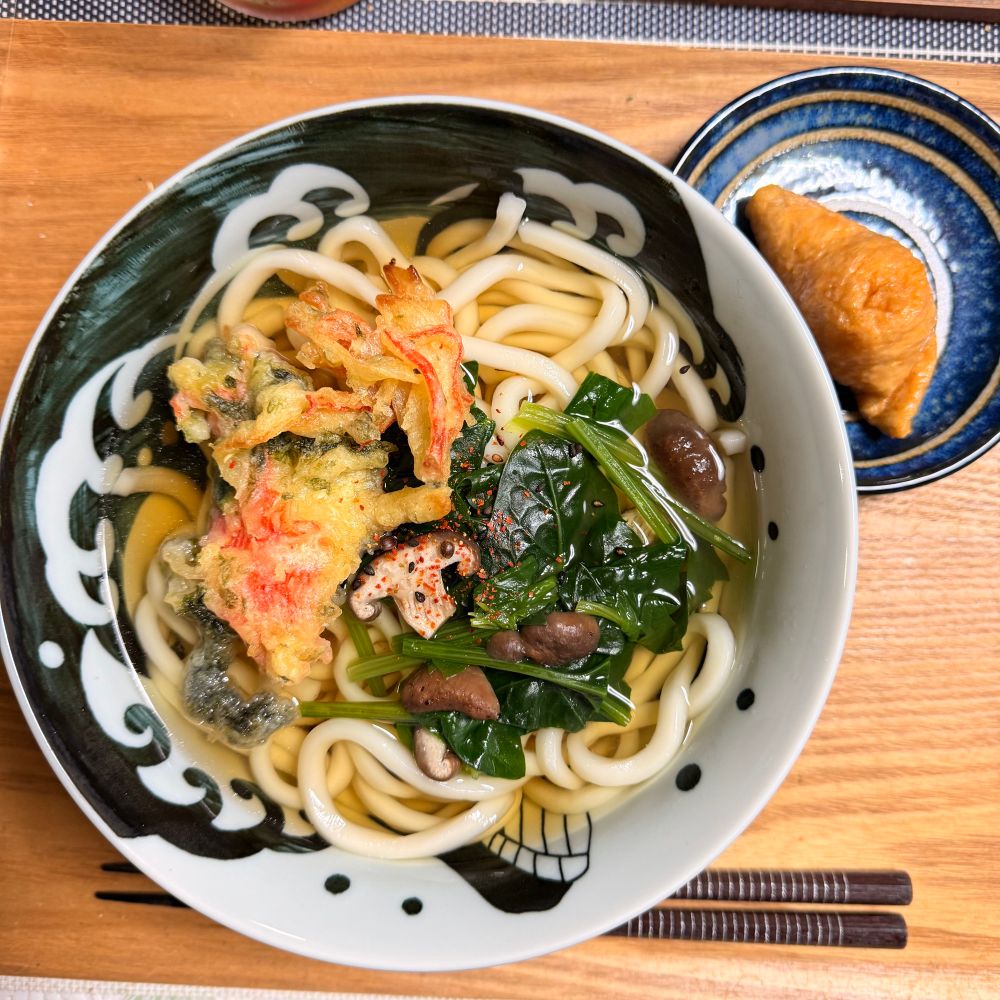 白波くじらのラーメン鉢にかけうどん。つゆにはほうれん草と椎茸が入っており、お惣菜のカニカマとあおさの天ぷらをトッピング。