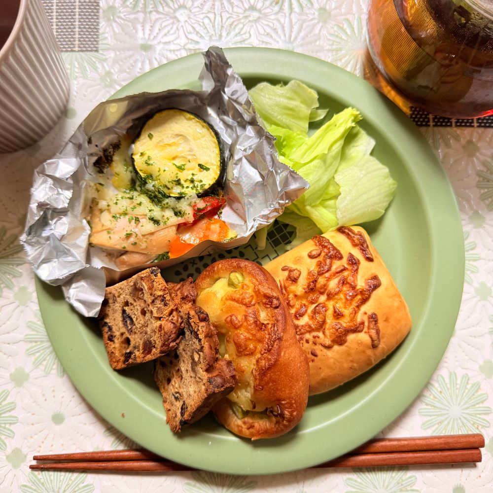丸い緑のトレイに、ナッツなどがたくさん入ったパンの端切れ、枝豆チーズ、ツナチーズのミニパン、ホイルを敷いた鶏もものレモン醤油焼き、ちぎったレタスが乗った朝食プレート。