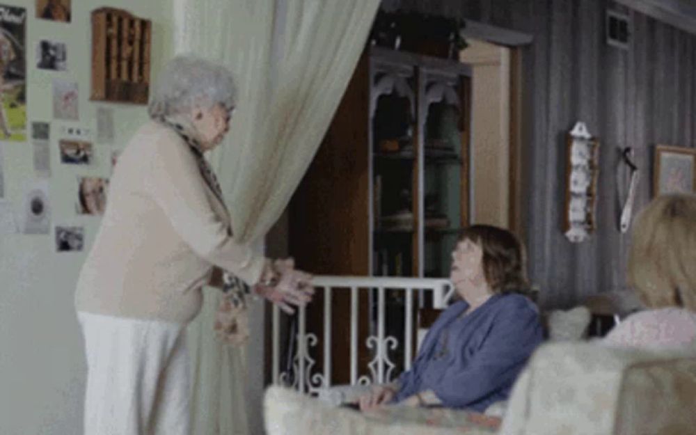 two elderly women are standing in a living room talking