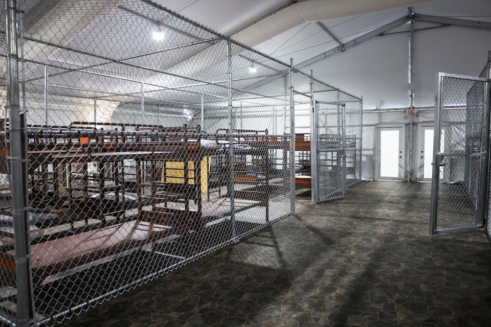 A tent structure with cages of chain link fencing, and basic bunk beds cramped together. 