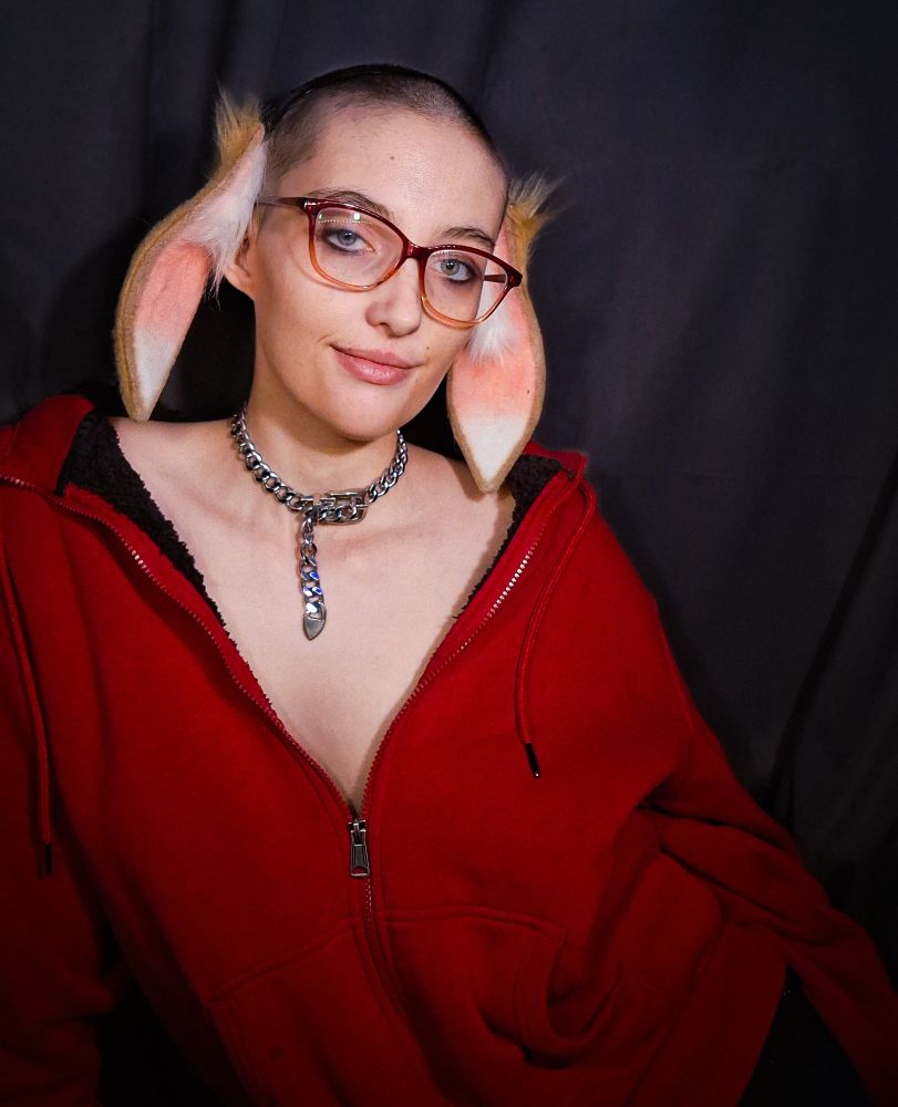 Person wearing a red jacket halfway unzipped, a chain collar, red glasses and lop bunny ears.