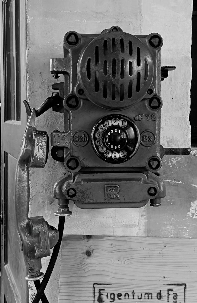 Schwarzes Wandtelefon mit Wählscheibe; die Klingel geschützt hinter einem Metallgitter, massiver Hörer zum einhängen 