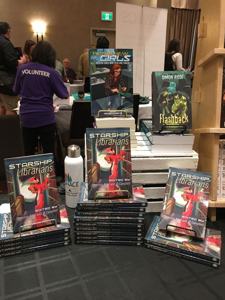 Book display at When Words Collide. There are three stacks of varying heights of Starship Librarians, an anthology. Behind the anthology, sitting on a crate, are two more titles for younger readers.