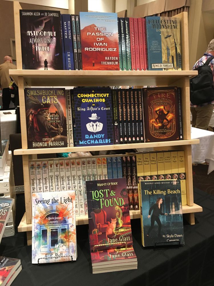 Book display at When Words Collide. A shelf of books full of sci-fi novels and anthologies; fantasy detective stories; fantasy anthologies; and paranormal crime books by E. C. Bell and Skyla Dawn Cameron.
