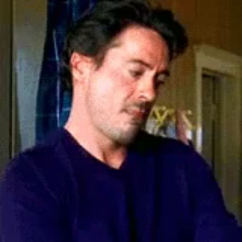 a man in a purple sweater is sitting in front of a window in a room .