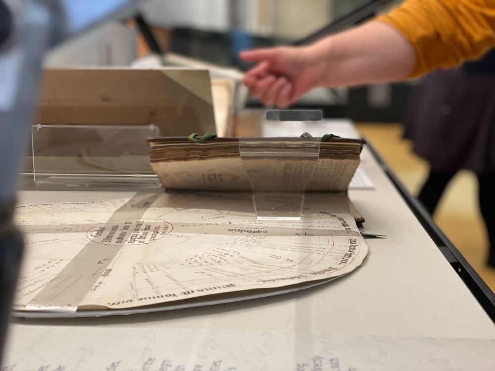 Image of open handwritten recipe books inside a display case. A hand in the background adjusts the pages. 