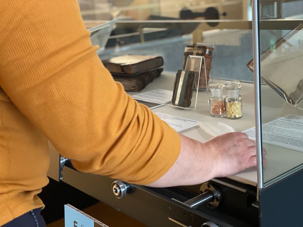 A member of staff places a quill into an open exhibition display case. 
