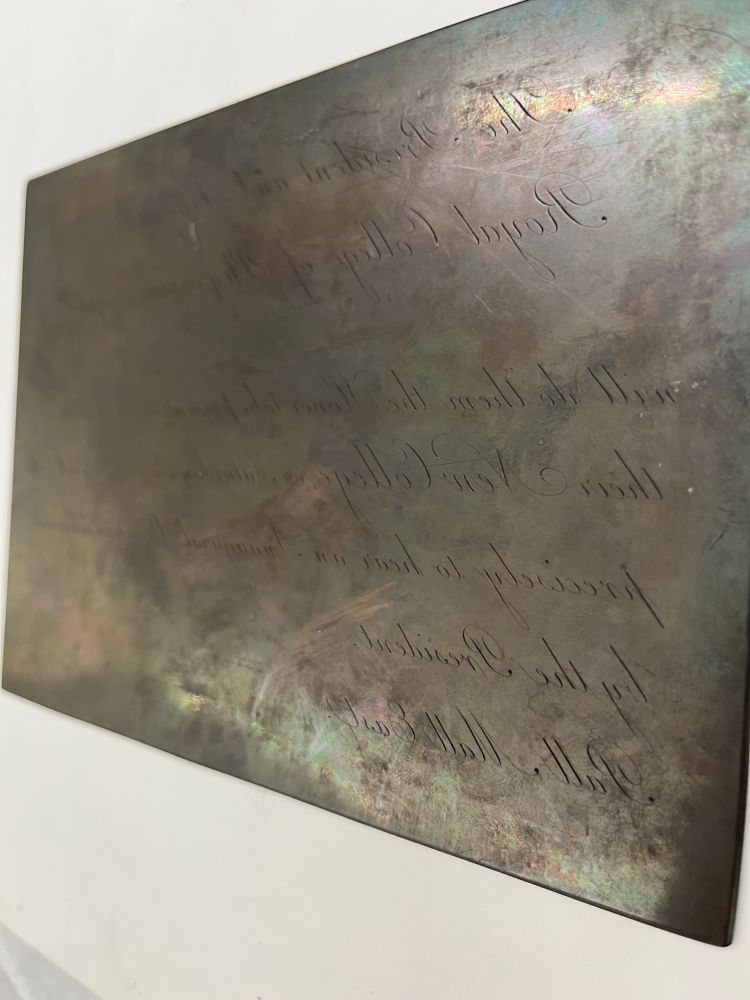 A copper plate with inscribed text. This is the original image of the plate so the text is in reverse to allow printing. 