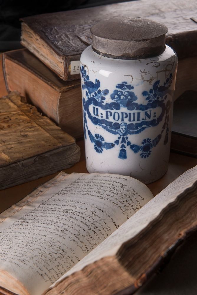 A blue and white ceramic apothecary jar with an open handwritten recipe book in front.