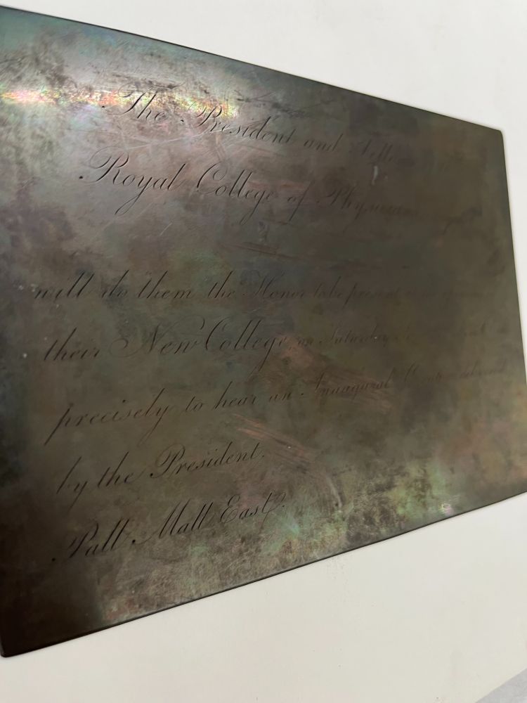 A copper plate with inscribed text. We have flipped this image, so you can read some the invitation. On the actual plate the text is in reverse to allow printing. Not all text is visible due to the shiny nature of the metal. Key words that can be seen read: 'The President', 'Royal College of Physicians', 'New College' and 'Pall Mall East'.