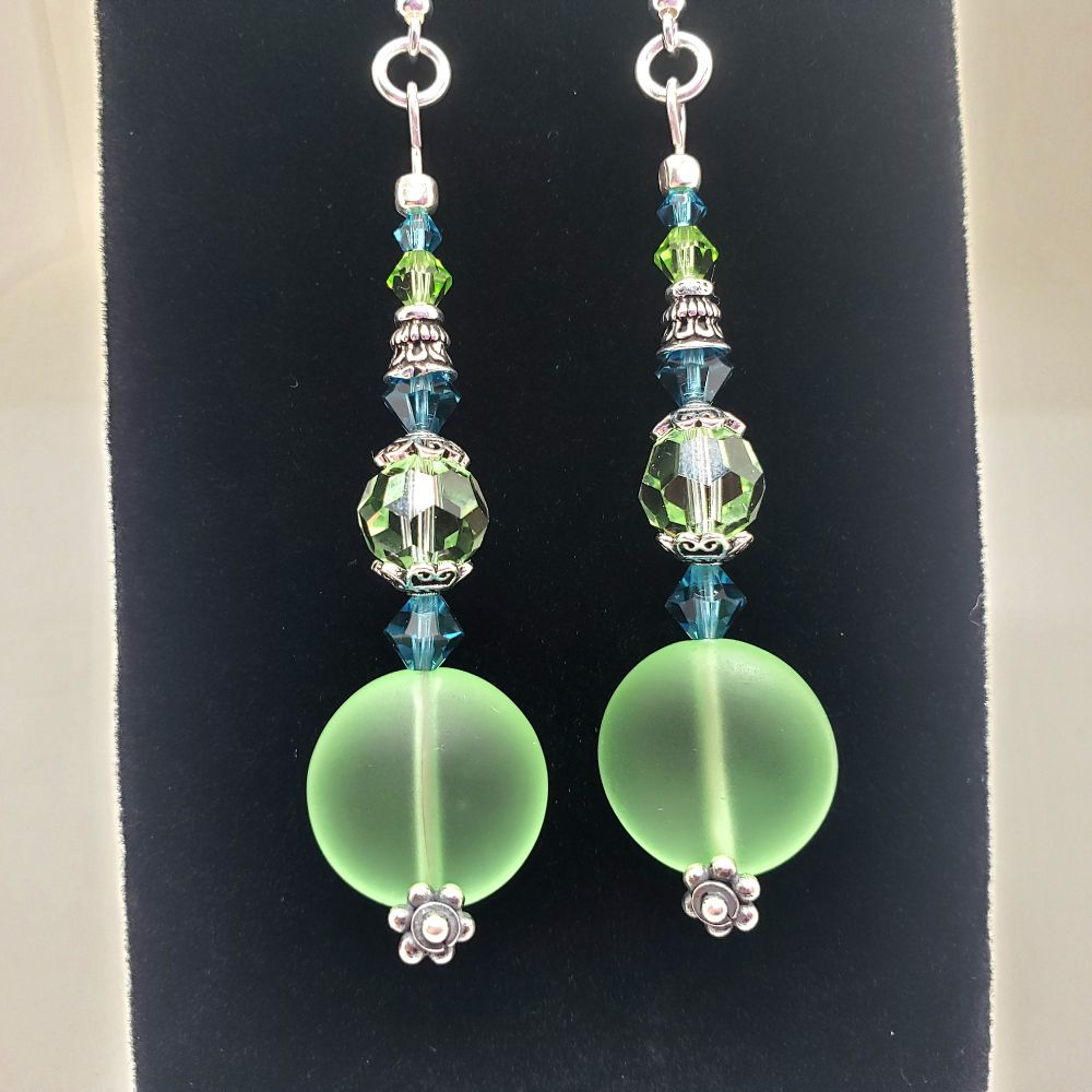Inspired by BTS Dynamite Concept Photos these earrings are handmade with 10 Genuine Swarovski Crystal Beads: 2 each 8mm Round Bead in Peridot, 2 each 4mm Bicone in Peridot, 4 each 5mm and 2 each 3mm Beads in Indicolite, 2 each 15mm man-made Light Green Sea Glass beads All silver components are .925 Sterling Silver. Approximately 2.75" long.