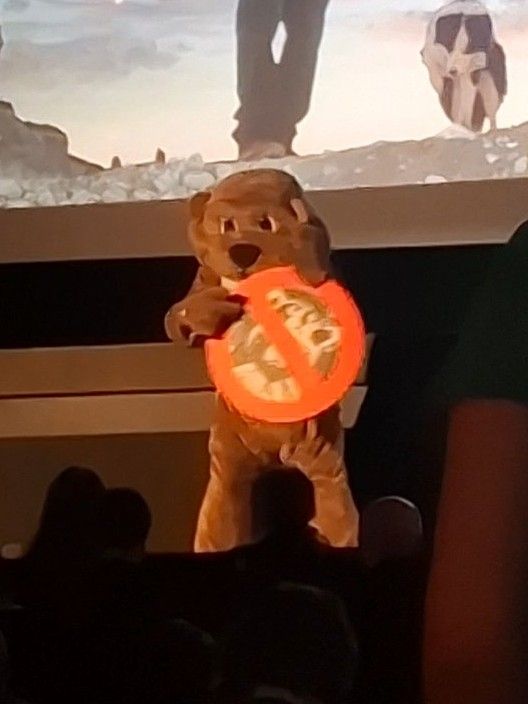 Person in beaver costume holding a sign with a big red line through man in racoon costume 