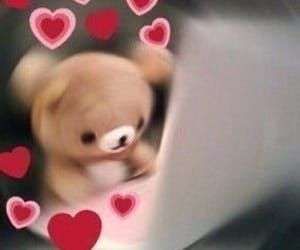 a teddy bear sitting at a laptop surrounded by a swirl of heart emojis