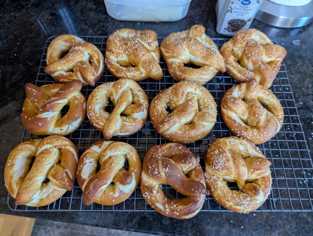 Picture of a wire rack with a dozen homemade soft pretzels. The pretzels are cracked and perhaps a bit light, but otherwise ordinary 
