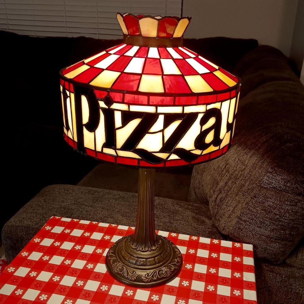 A stock photo of a Tiffany style lamp that says Pizza Hut on it (only Pizza is visible). The lamp has red and white checkers and is on a red gingham tablecloth.