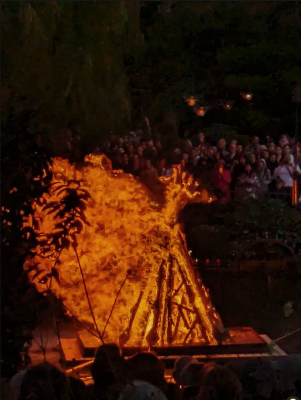 Giant bonfire, flames billowing in the wind. The back of one of the heads is Mette Frederiksen.