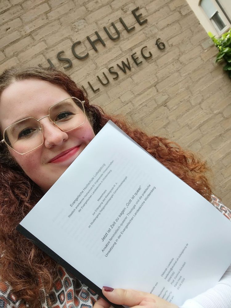 Ich grinse in die Kamera. Zeige dabei meine gebundene Masterarbeit.