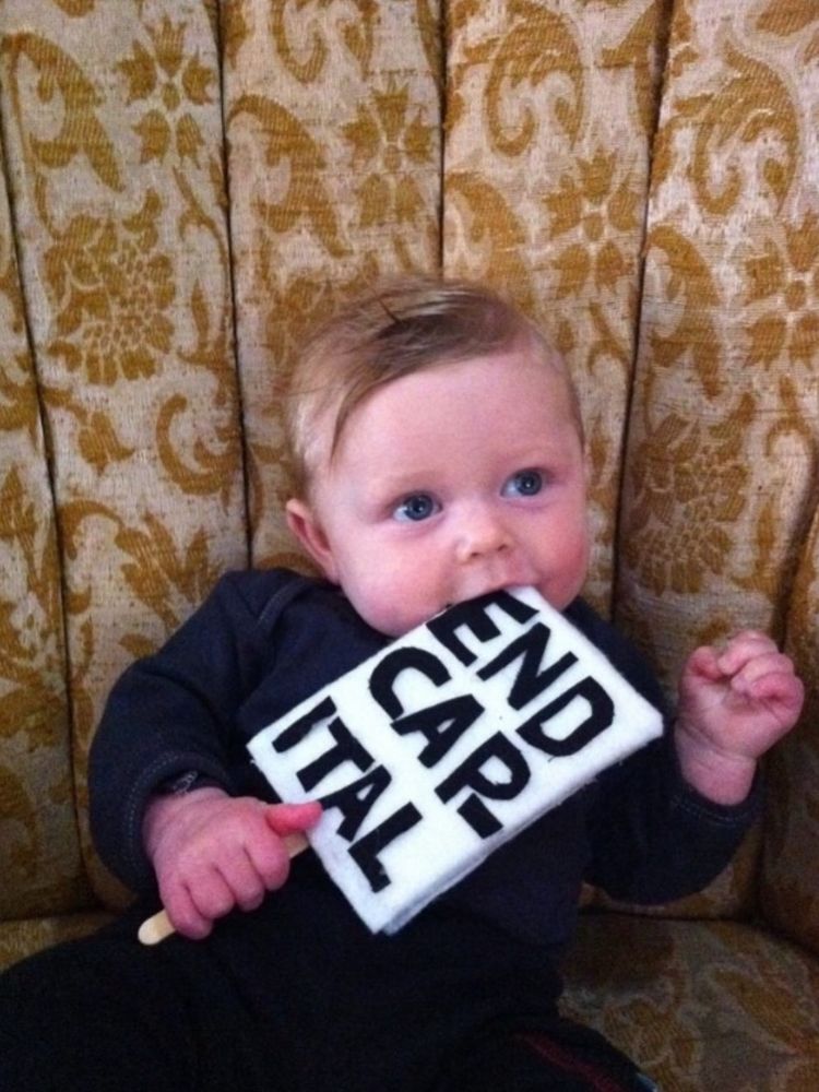 Baby holding a sign that says “end capital”