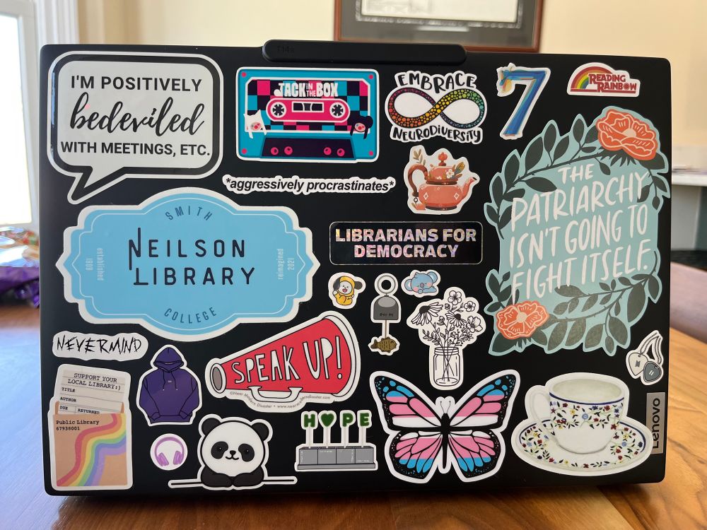 A photo of a laptop covered in stickers I closing many BTS images, a tea cup, library stickers and more. 