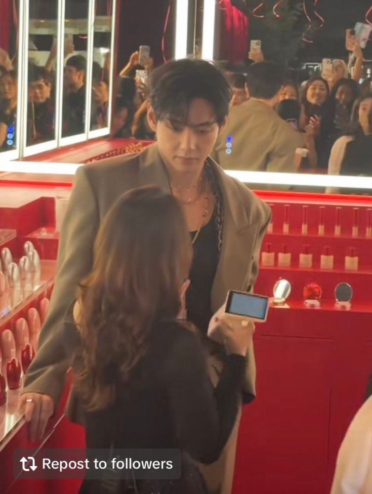 Taehyung at Tirtir pop-up. A woman is explaining the products to him, and he's listening while Towering over her