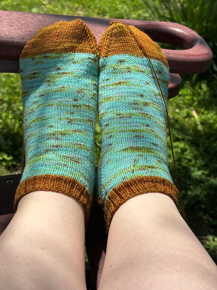 Lucy, a fat white person, wearing aqua and brown hand knitted socks.