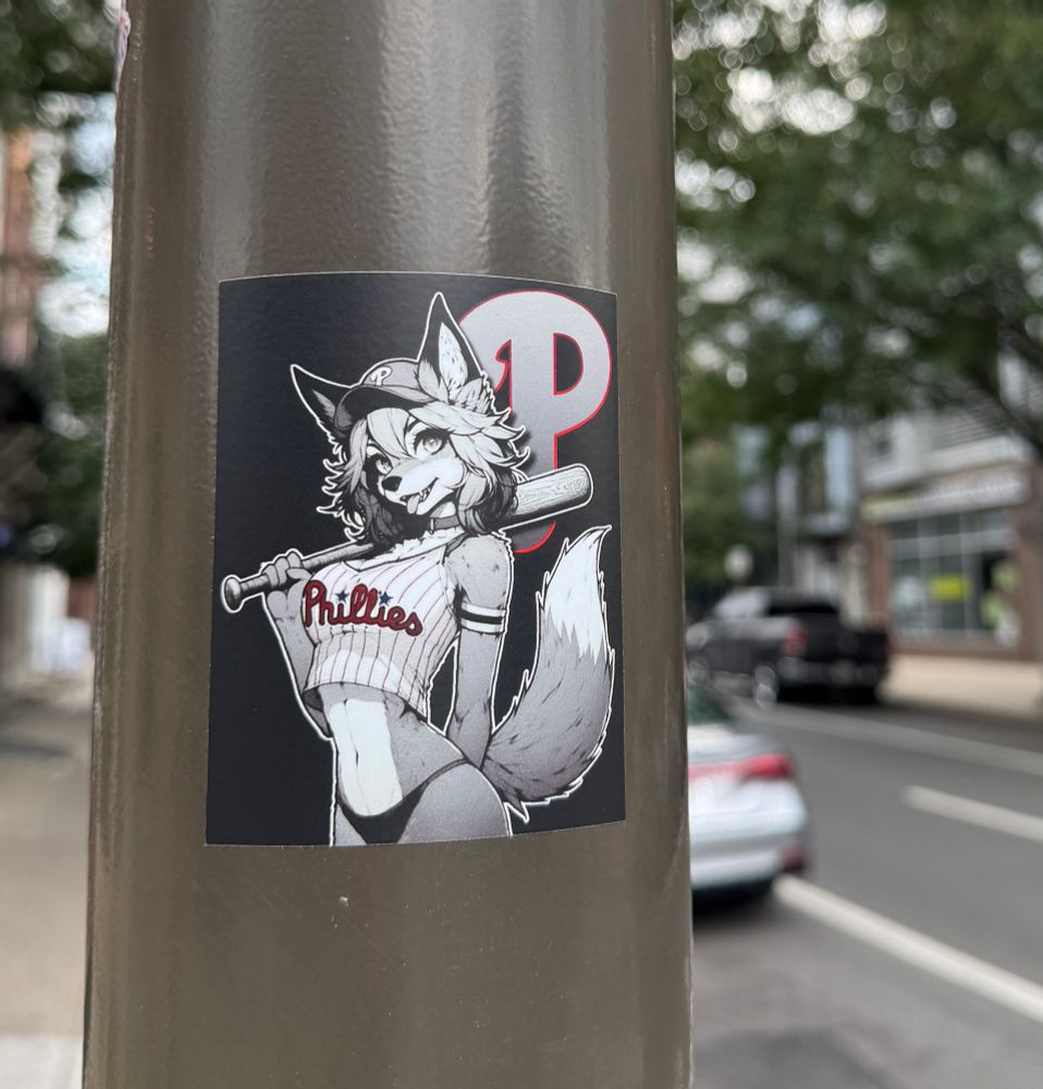 A sexy fox has a Phillies jersey crop top with the Phillies p in the background. She’s holding a baseball bat. 