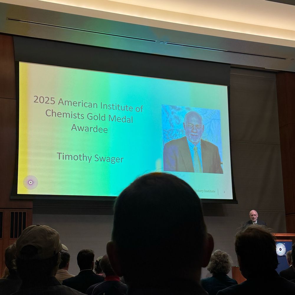 A comically shitty picture of a man at a podium talking in front of a slide with his name and face on it. It says Timothy Swager and 2025 American institute of chemists gold medal awardee 
