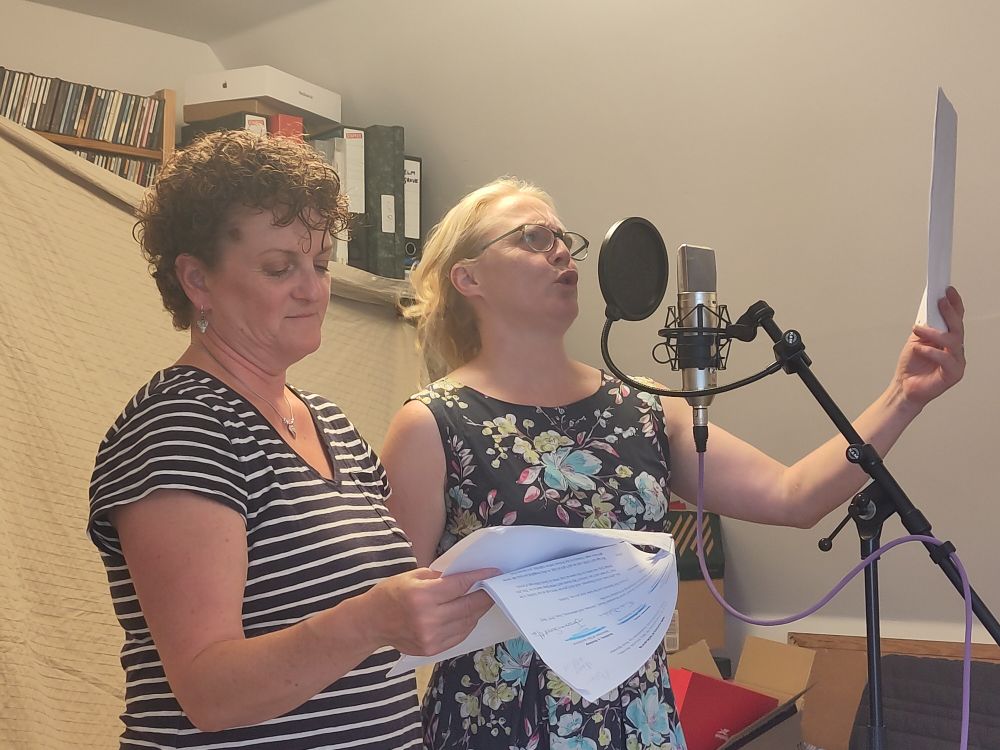 Two ladies sharing a mic and reading the same script of dubious quality. One of them is really giving it some beans. 