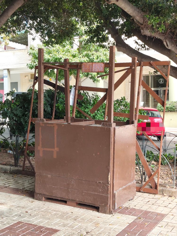 Un pequeño puesto de castañas asadas en marrón sitiado en la calle con las ramas de un árbol por encima. El puesto está sin personas pues simplemente acaban de dejarlo alli. 