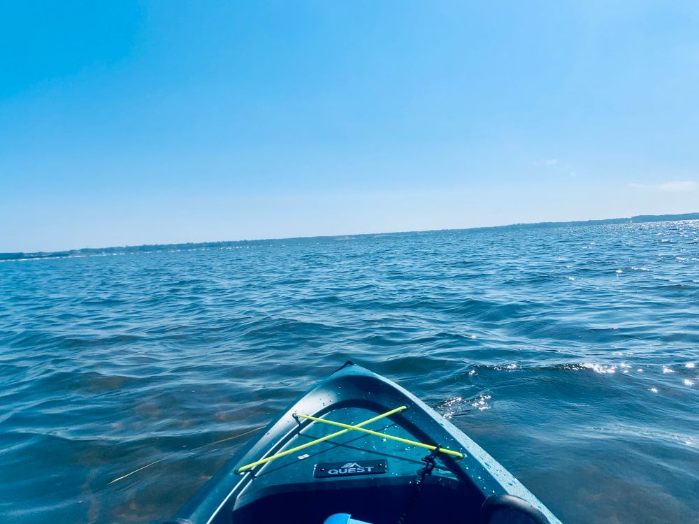 Photo of the expanse of Muskegon Lake (Muskegon, MI) with the far shore just at the edge of the horizon; in the foreground the bow of a kayak is visible.