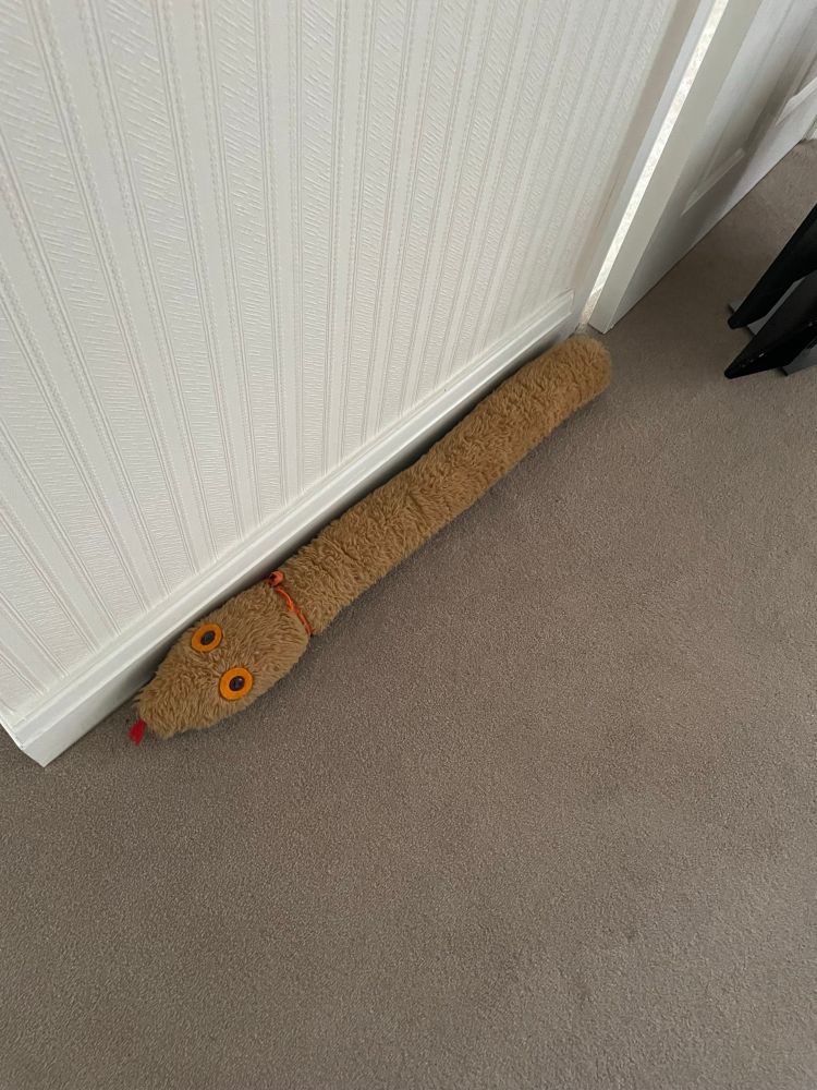 A light brown draft excluder shaped like a snake with a little red blem tongue. 