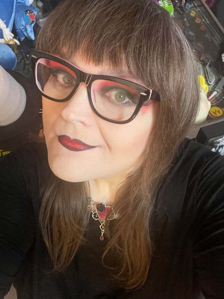 Stephanie Sterling with red/black eyeshadow and red lipstick lined with black. Wearing a red heart necklace and black top.  