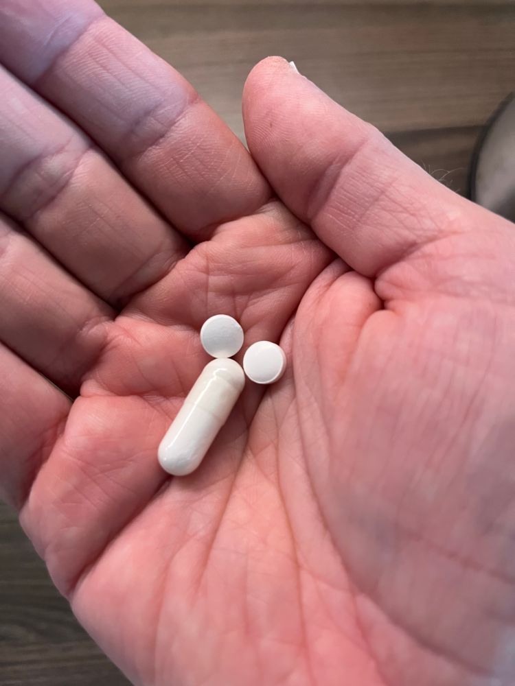 Tre tabletter i en hand, två vita runda och en lång cylindrisk, ordnade för att likna ett könsorgan