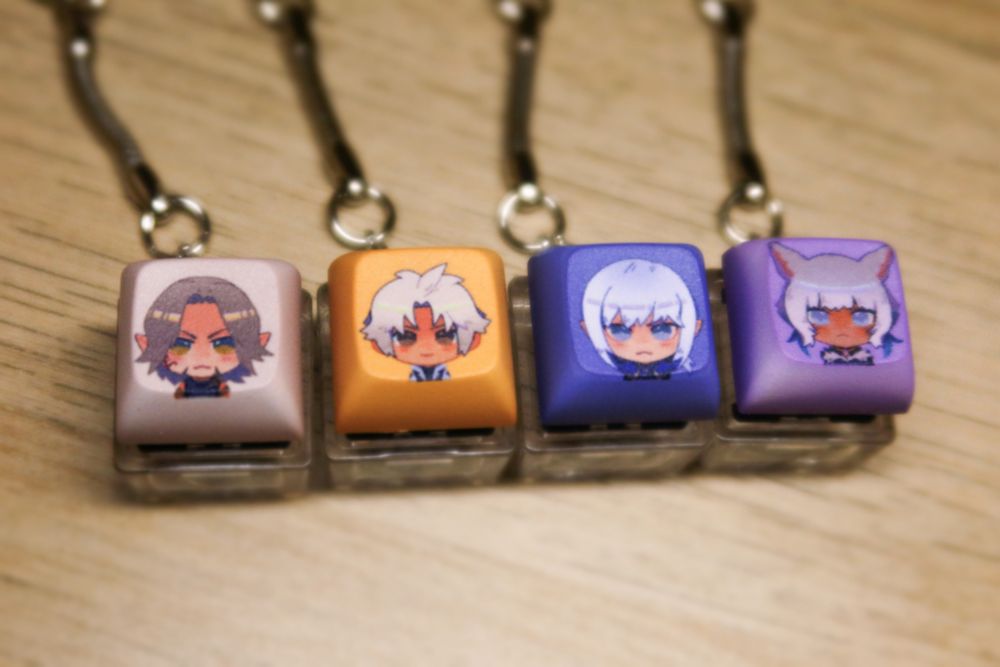 (from left to right) keycap keychains featuring Urianger, Thancred, Estinien, and Y'shtola from FFXIV
