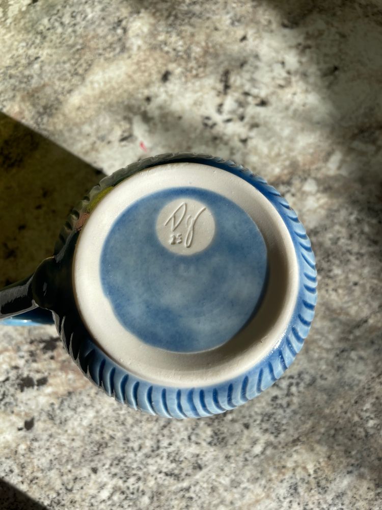 The bottom of the light blue mug. The foot ring is glazed inside, with an unglazed circle showing the makers mark DG 25