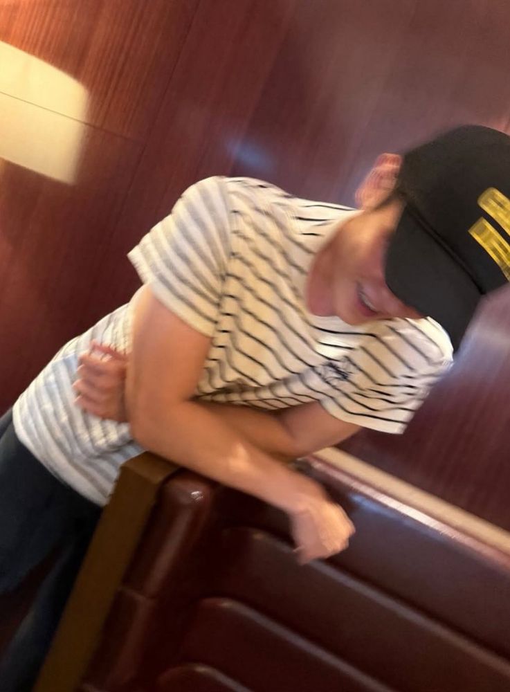 Blurry photo of Taeyong leaning forward against a restaurant booth. His forearms are resting on the top of the booth and he’s smiling. 