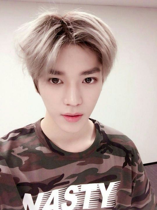 A selfie of Taeyong. He’s wearing a camo print t-shirt that says NASTY in white letters across the chest.  
