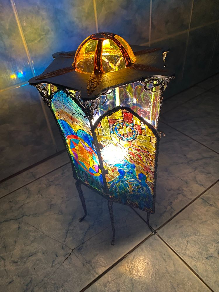 A lantern with a stained glass that has sun and two angels on it. Standing on 6 legs with small paws. With an open door