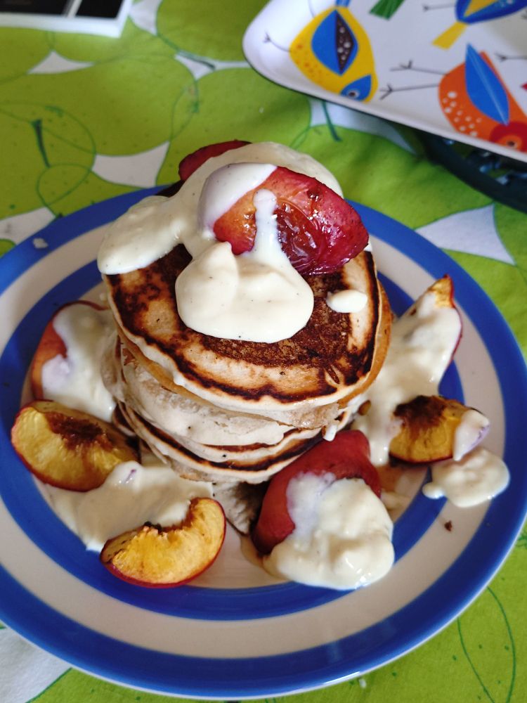 Stack of American style pancakes on a blue and white plate, with roasted nectarines, maple syrup and vanilla yoghurt