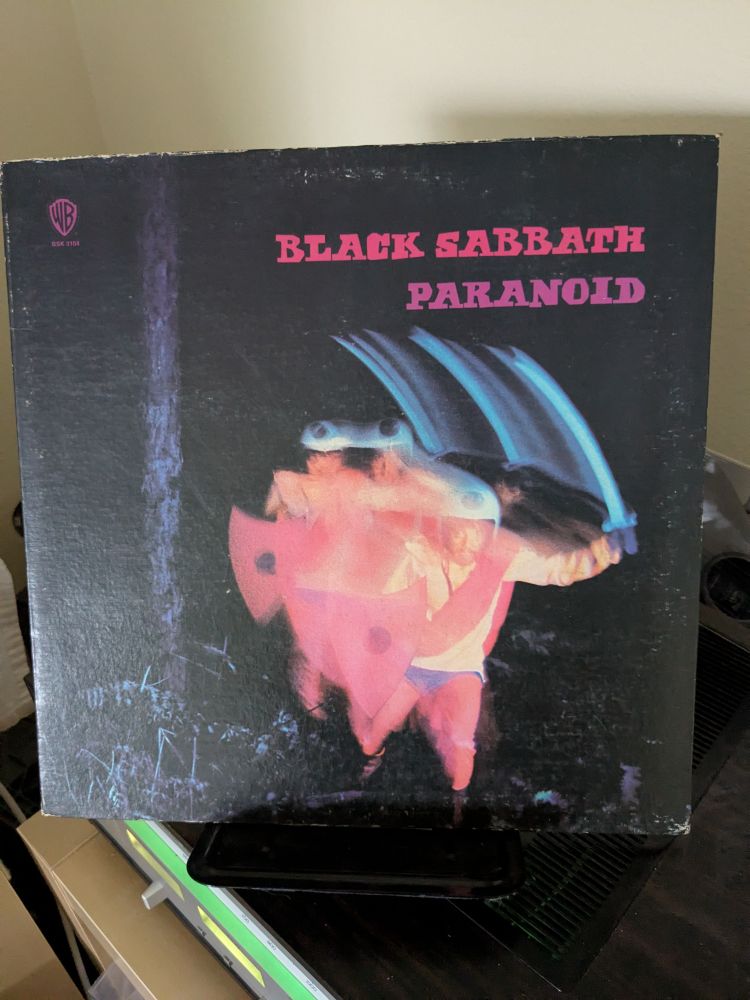 Album cover for Black Sabbath: Paranoid pictured is a weird dude in a helmet with a shield and a sword at night in the woods. Weird guy pictured is blurred 