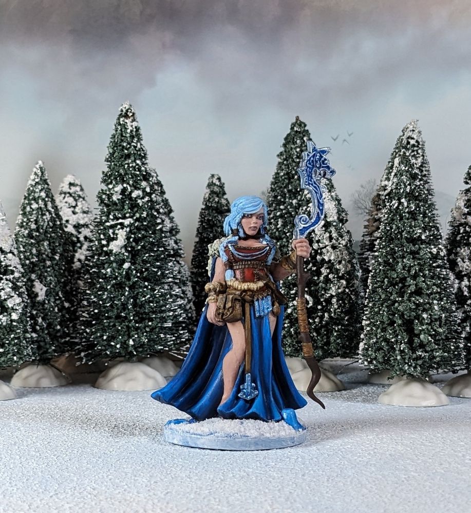 Painted Frost Giant Queen miniature with snowy pine trees in the background. Front view.