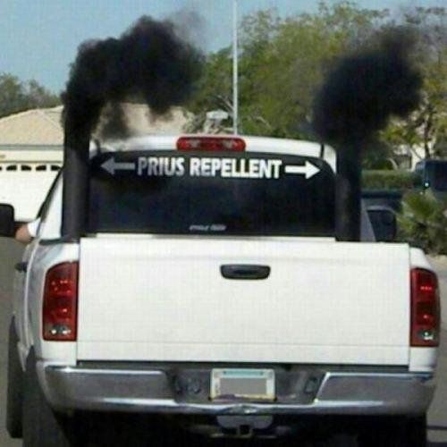 Photo of a diesel pickup with twin vertical exhaust pipes like a big rig, belching thick black smoke. A sticker on the rear window reads 'PRIUS REPELLENT'