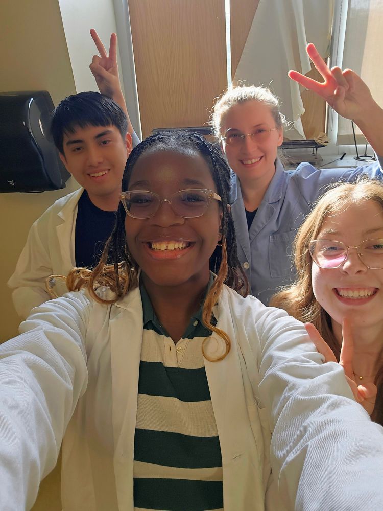 A selfie of microbiology students Delivrance (holding phone), Ivanna, and Adrian with myself in the back giving bunny ears to Ivanna and Adrian. 