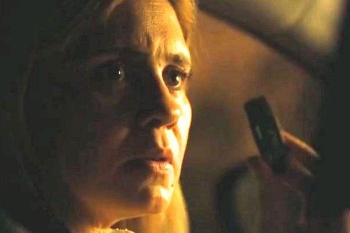 Um frame com uma mulher loira com cara apreensiva olhando provavelmente para alguém, com luz amarela dramática que cobre só um lado do rosto. Ao fundo, uma mão segura um pen drive.