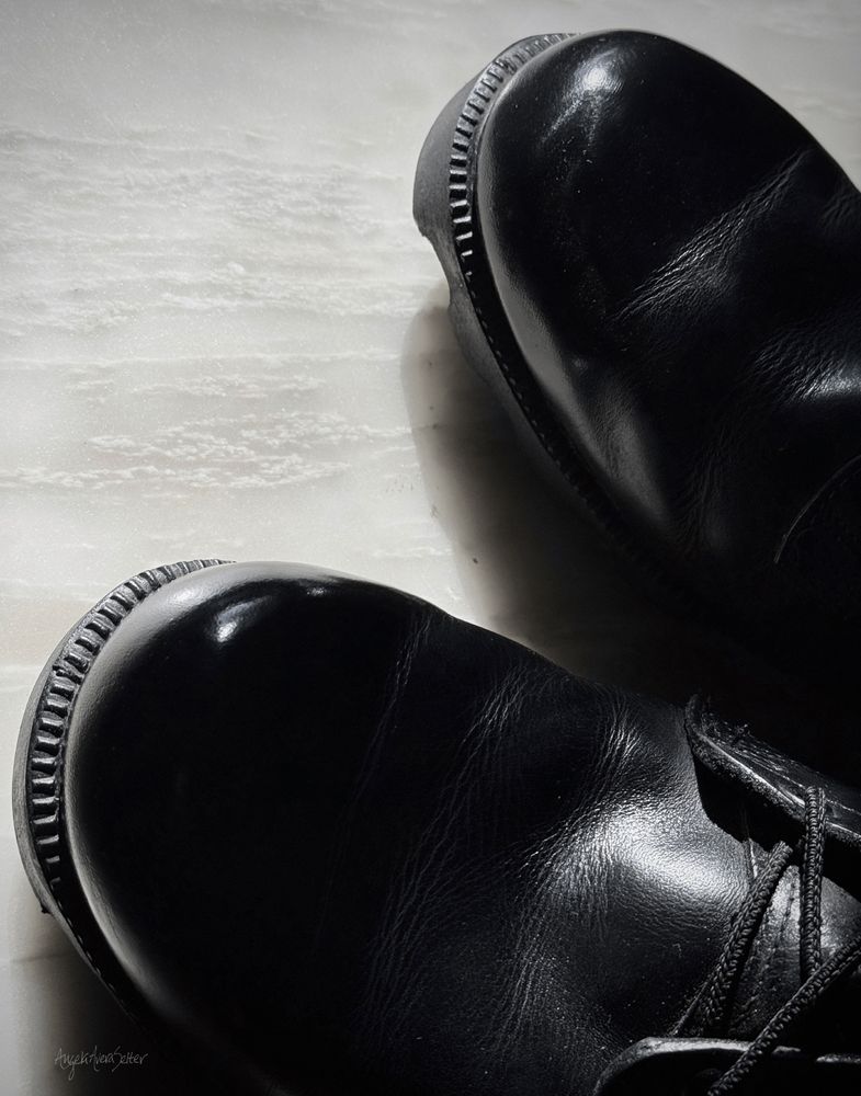 Monochrome photo. Toes of black leather Army boots on a white marble floor. The toes are spit-shined to a high gloss. 