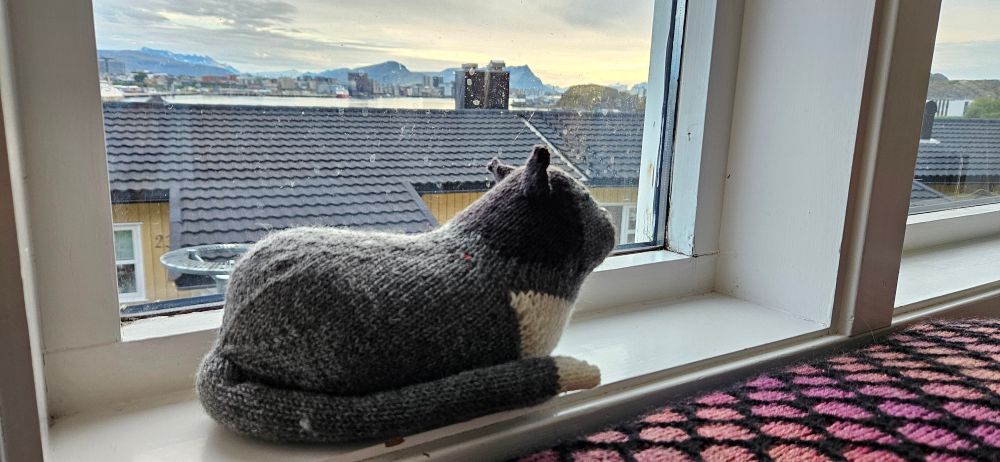 Grey knitted cat on a white window sill.