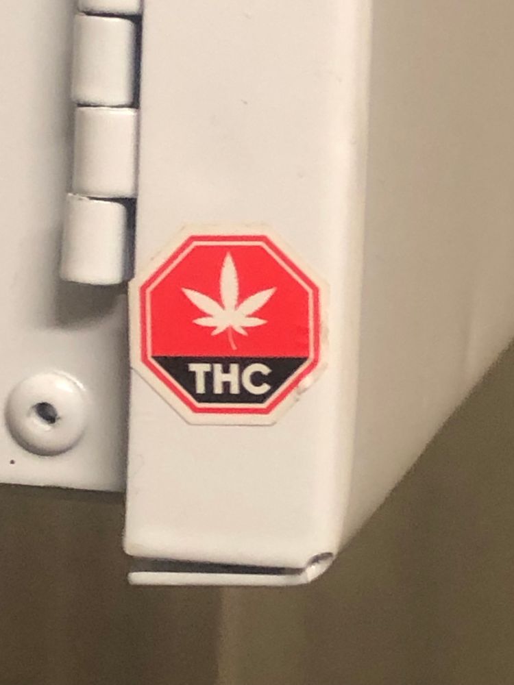 a octagonal THC aticker indivating a product containing thc and inapected in Canada, stuck to a white metal hinged door. 